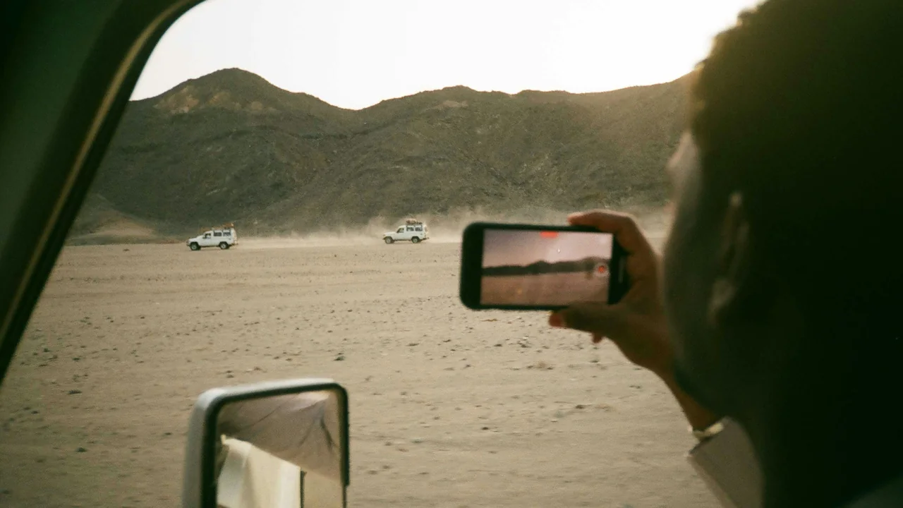 Person fotografiert die Wüste mit dem Smartphone aus dem Autofenster bei Marsa Alam