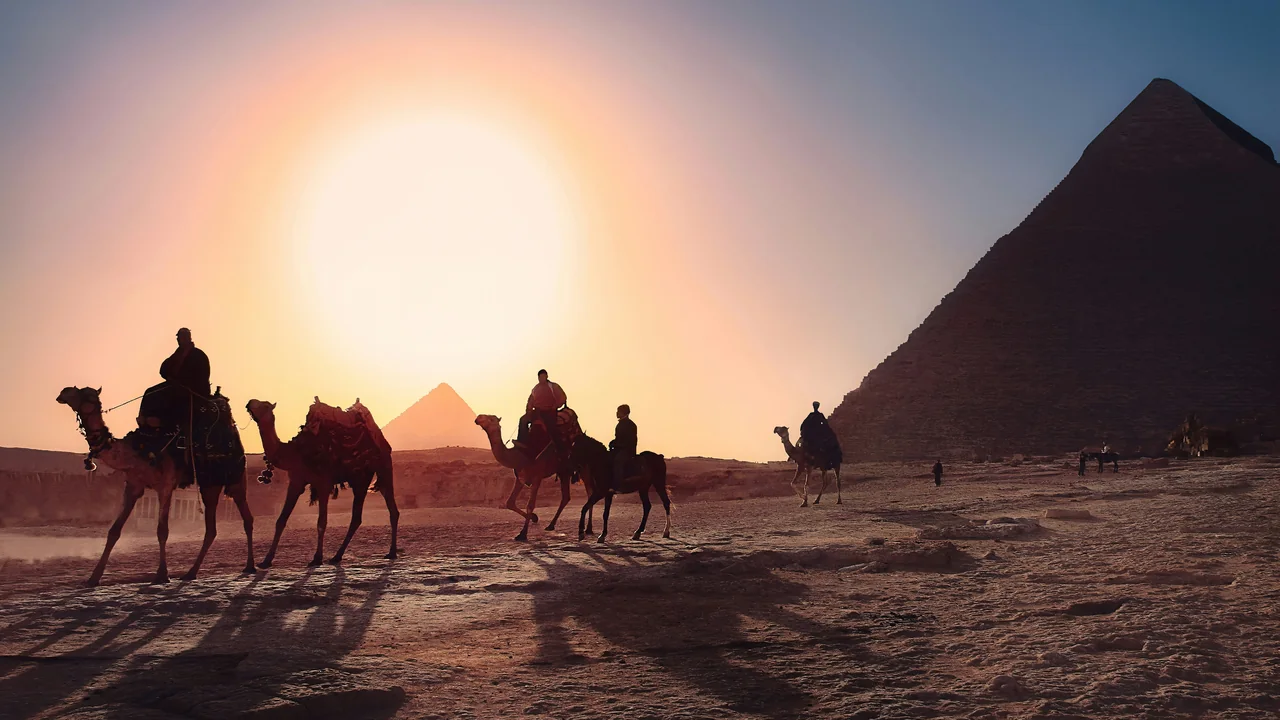 Reiter auf Kamelen vor einer Pyramide in Gizeh bei tief stehender Sonne